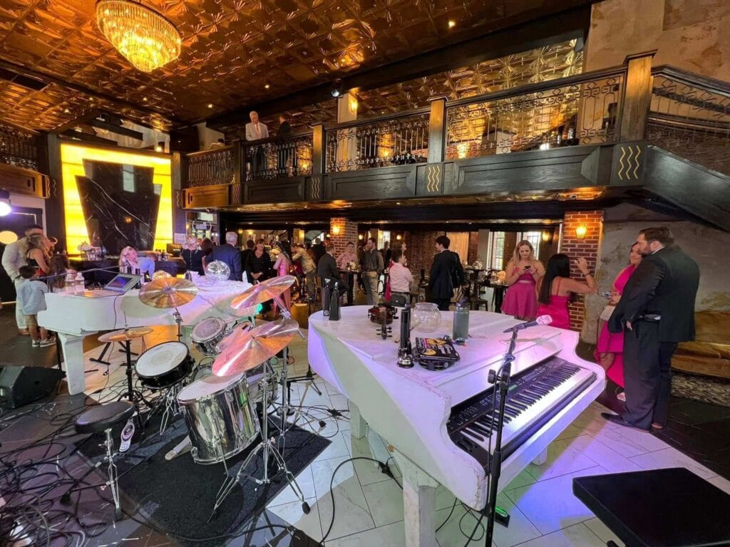 Dueling Pianos Official Road Show California Coast Edition setup with white pianos and drums at an elegant California wedding reception.
