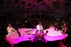 Actual Talent Dueling Pianos A man sitting on top of a piano in front of a crowd.